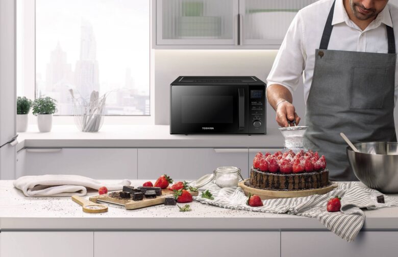 Mikrofalówka Toshiba stoi na blacie, na pierwszym planie mężczyzna dekoruje tort